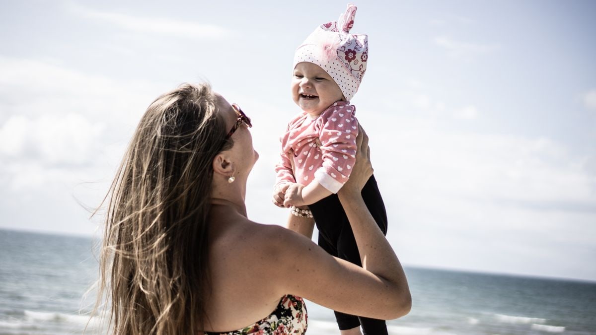 A happy mother lifting her smiling baby against a scenic beach backdrop.